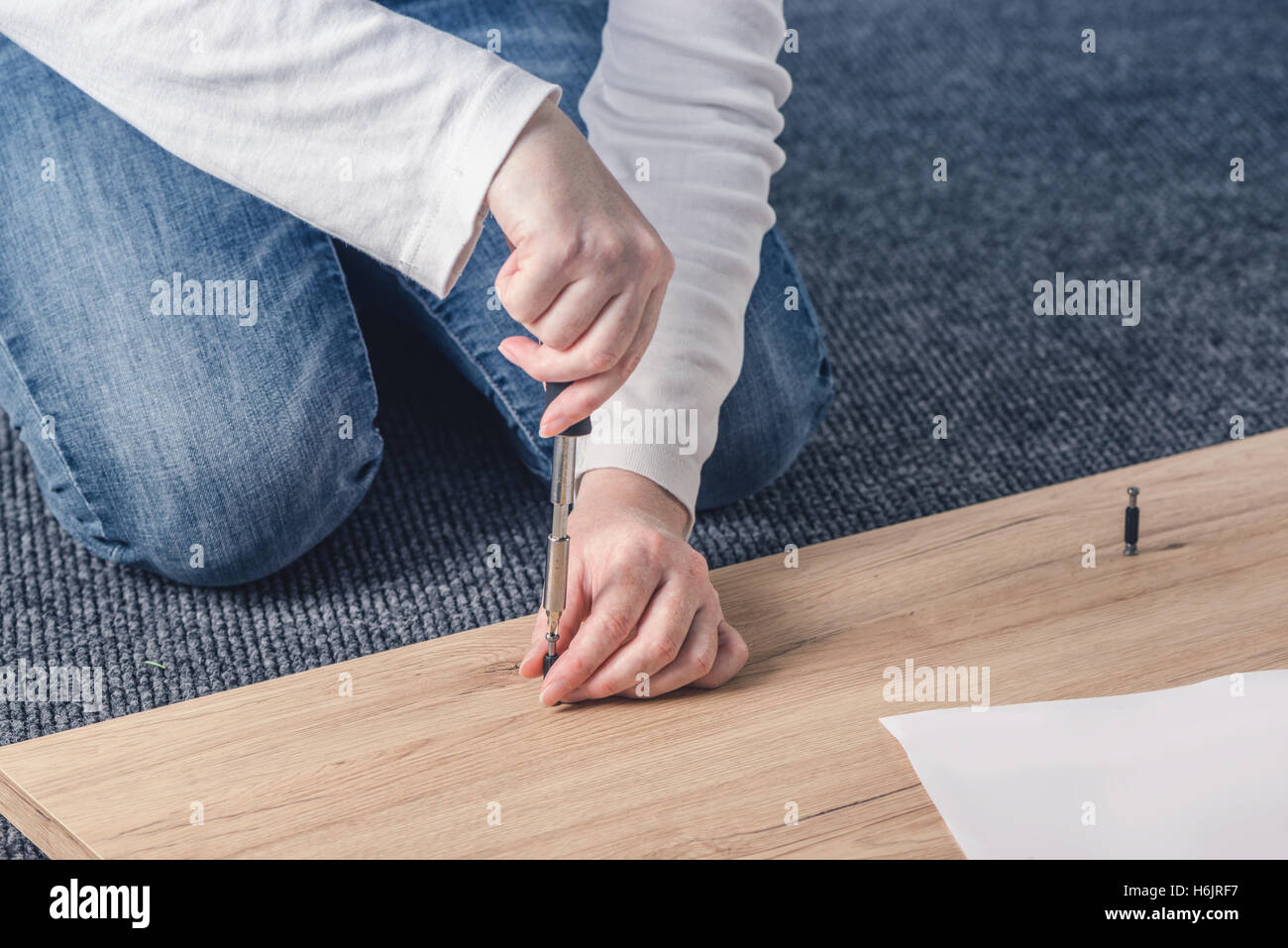 Donna di assemblaggio di mobili a casa sul pavimento, a mano con un cacciavite Foto Stock