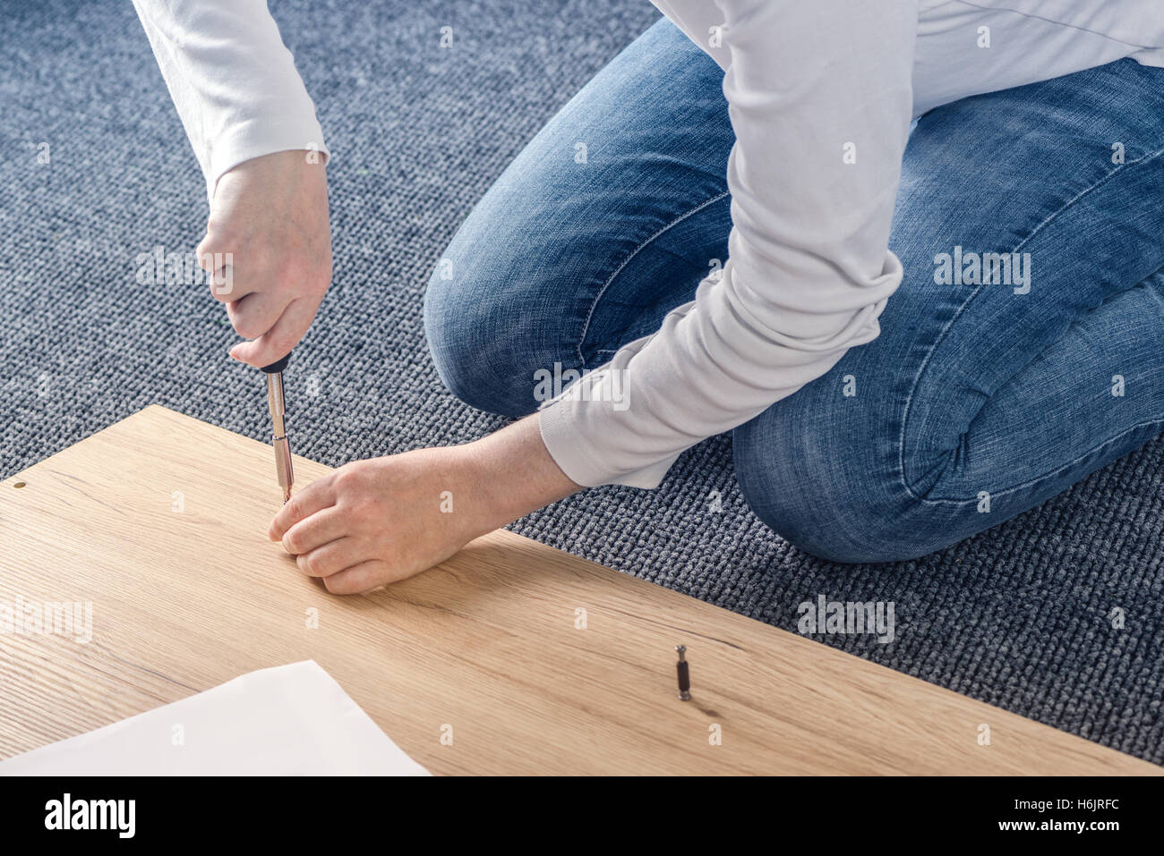 Donna di assemblaggio di mobili a casa sul pavimento, a mano con un cacciavite Foto Stock