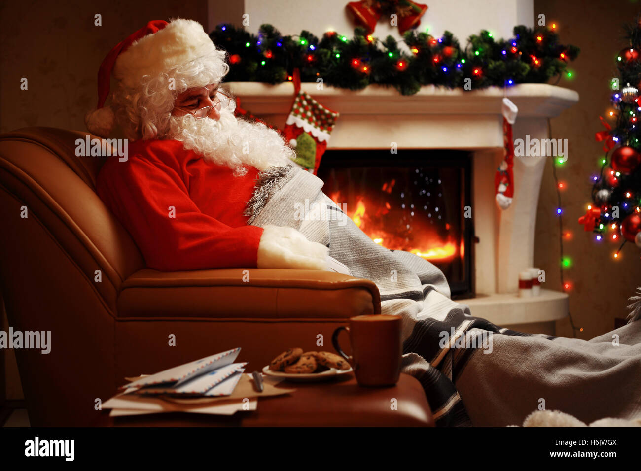 Santa Claus avente un periodo di riposo in una sedia confortevole vicino al caminetto a casa Foto Stock