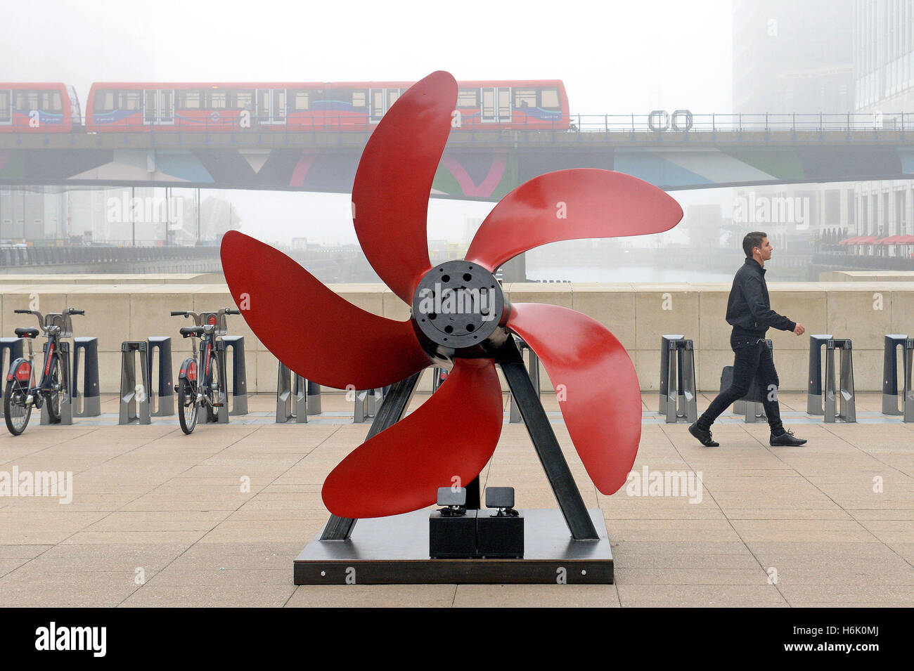 Un uomo cammina passato un papavero astratto dall'artista Marco Humphrey come parte del ricordo Art Trail a Canary Wharf, Londra. Foto Stock