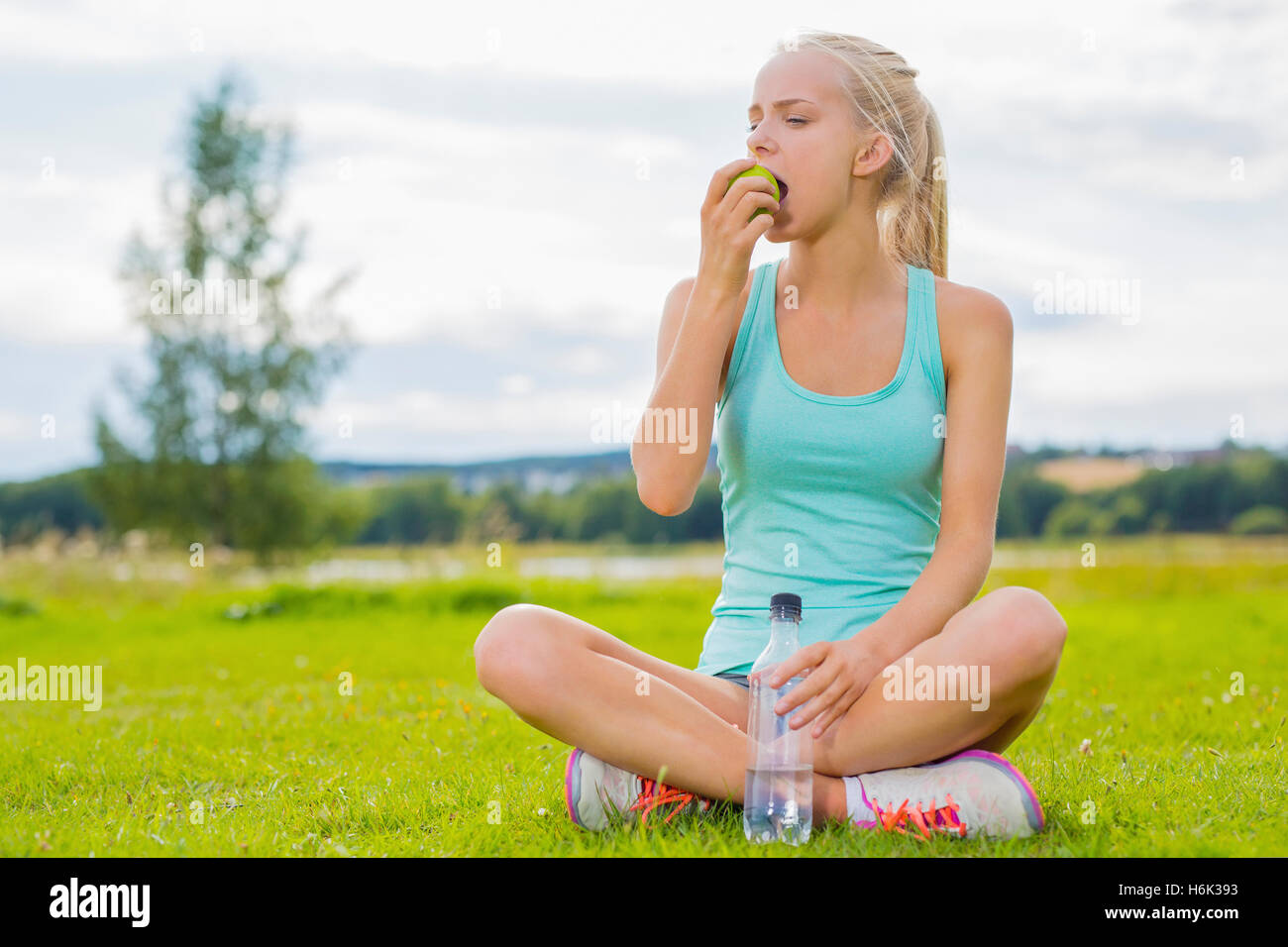 Donna seduta presso l'erba e mangiare apple dopo allenamento Foto Stock