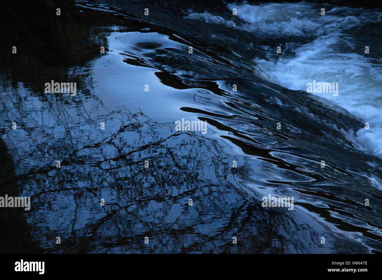 Blu scuro acqua nera passando al di sopra di uno stramazzo Foto Stock