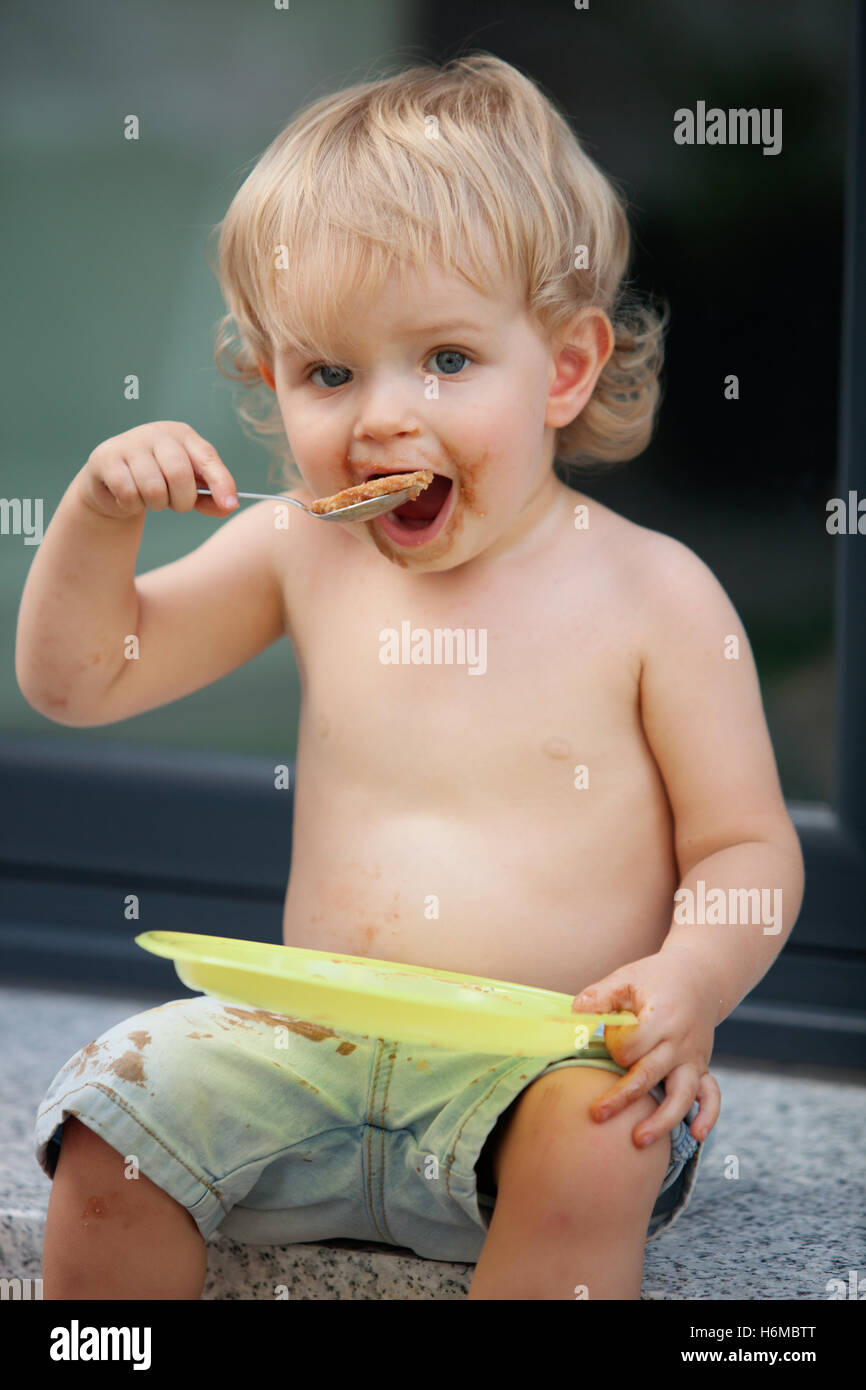Felice ragazzo di mangiare una torta al cioccolato su una piastra di colore giallo Foto Stock Felice ragazzo di mangiare una torta al cioccolato su una piastra di colore giallo Foto Stock