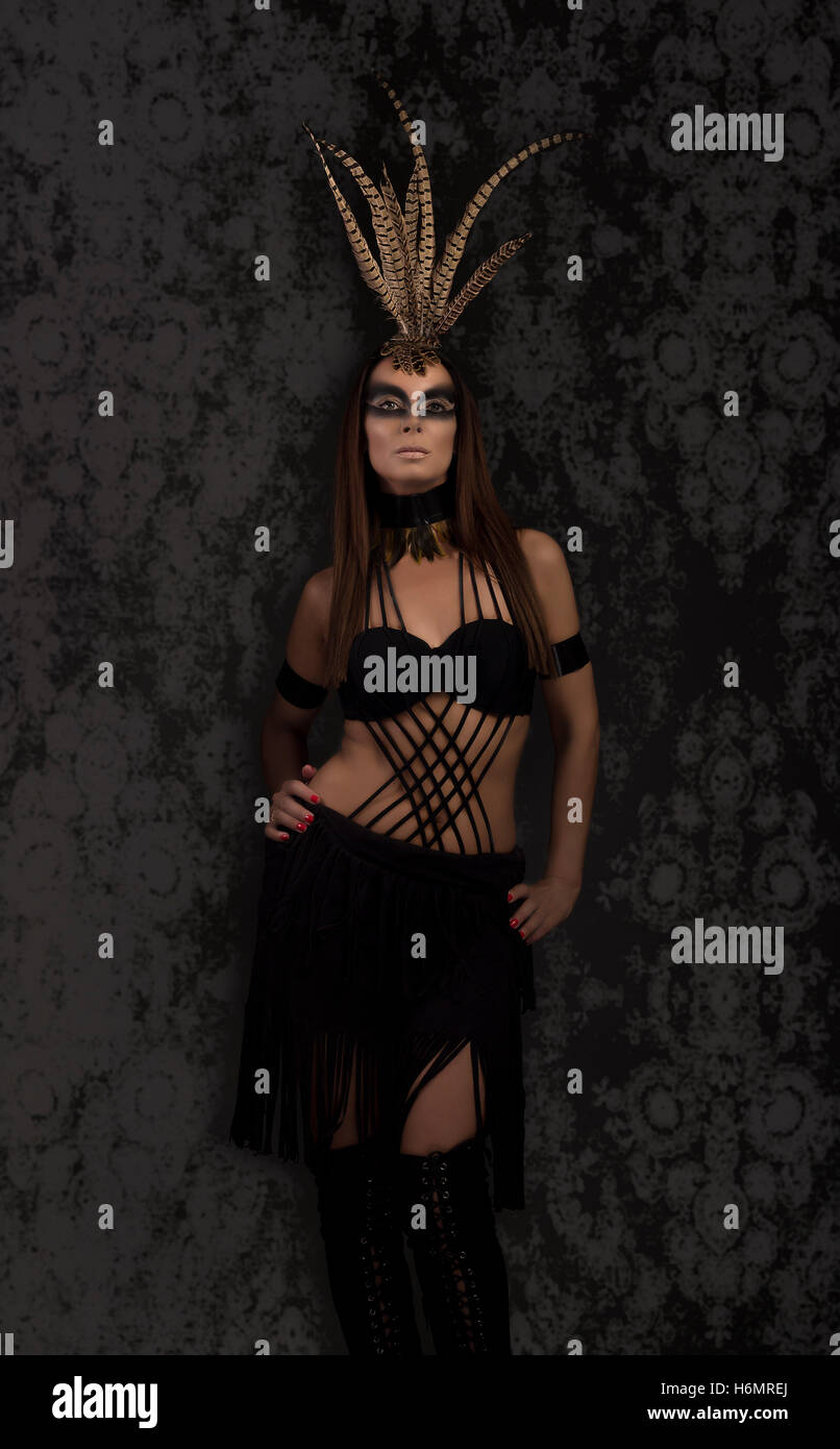 Conciate modello femminile in amazzonia stile supereroe vestito con copricapo di piume, nero sullo sfondo di Damasco Foto Stock