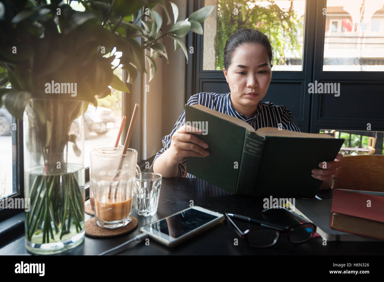 Domenica mattina scena dello stile di vita dei giovani hipster donna asiatica la lettura di libro in cafe con. Fine settimana di attività o hobby concept Foto Stock