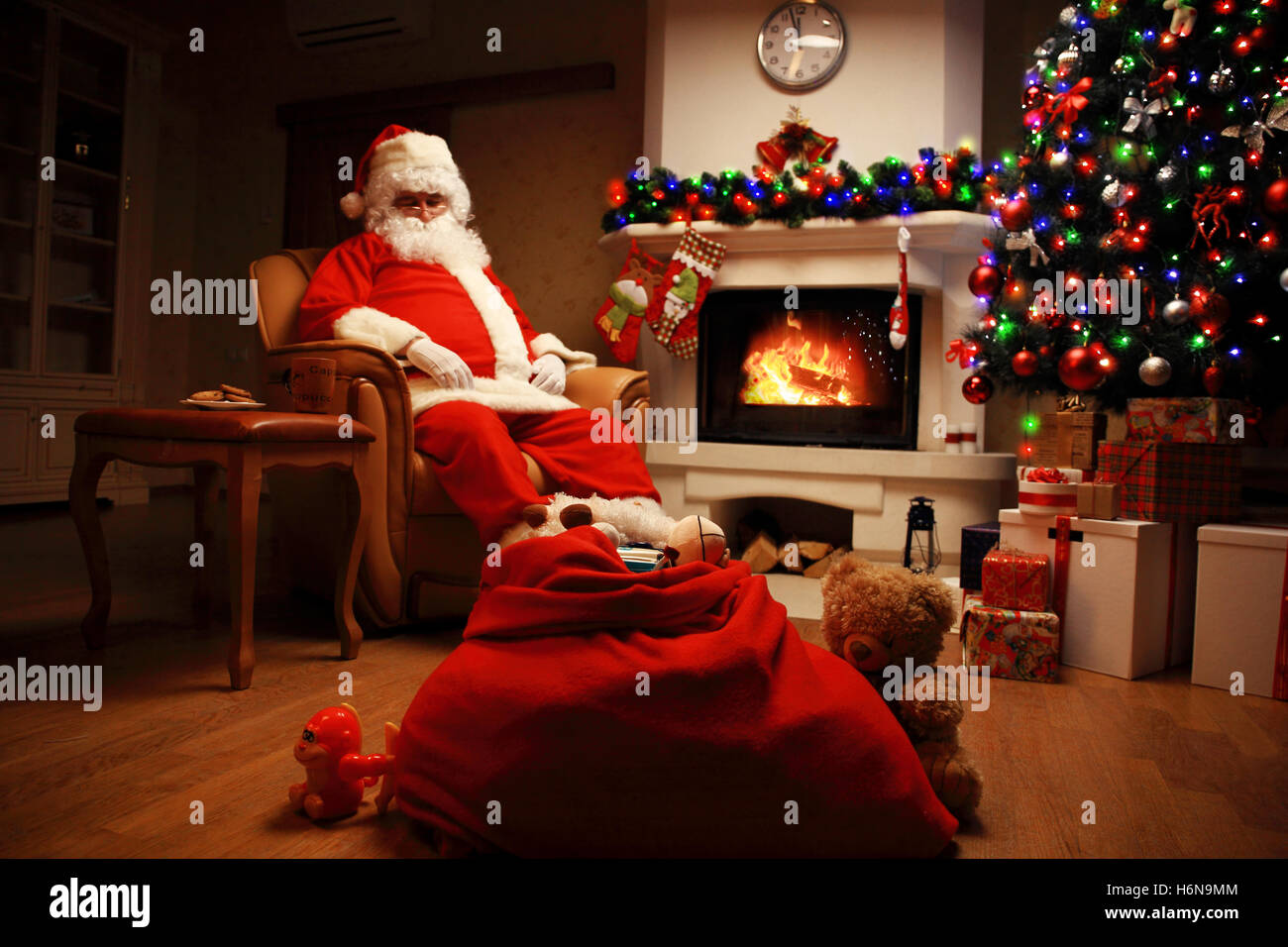 Santa Claus avente un periodo di riposo in una sedia confortevole vicino al caminetto a casa Foto Stock