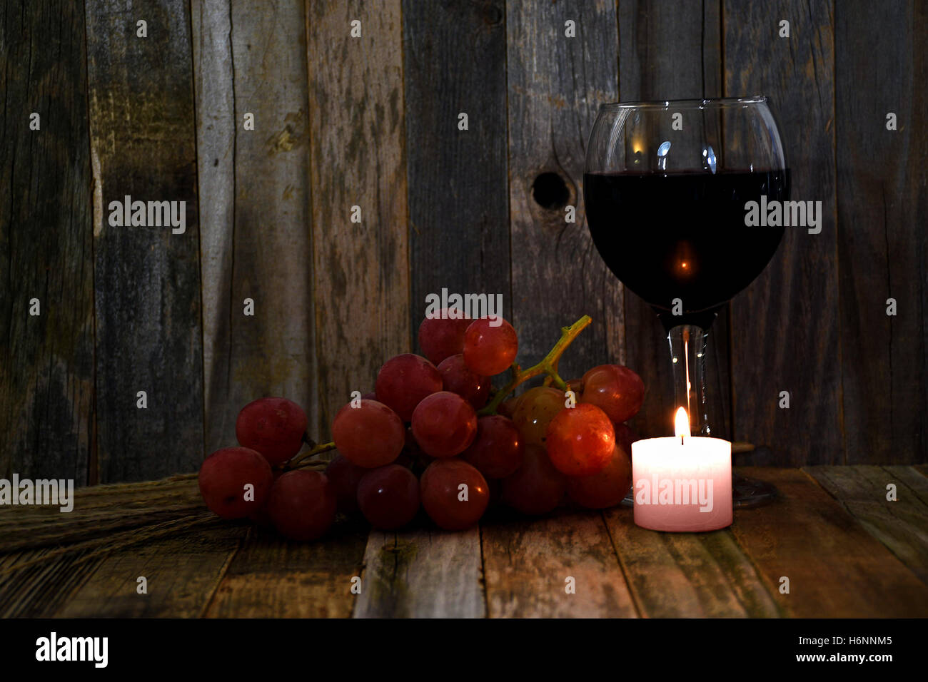 Vino rosso in vetro con uva e candela incandescente su legno rustico Foto Stock