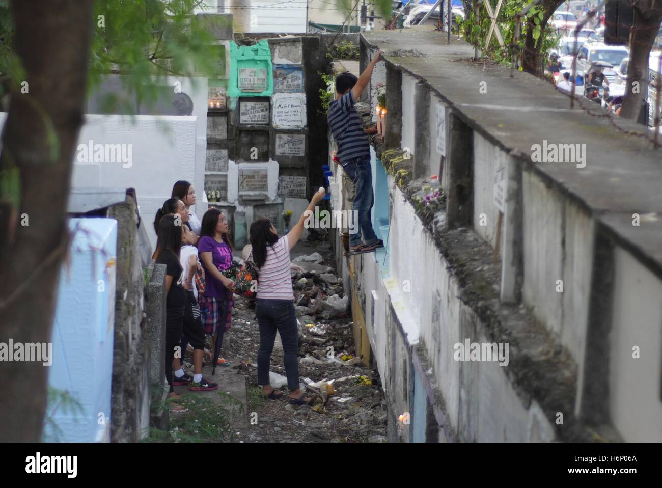 Makati, nelle Filippine. 31 ott 2016. Nel tardo pomeriggio la gente visita i loro cari defunti questa famiglia di cari grave è alta sul terzo livello mentre questo uomo sta cercando posto le candele e fiori una giovane donna è aiutare lui. Credito: George Buid/Pacific Press/Alamy Live News Foto Stock