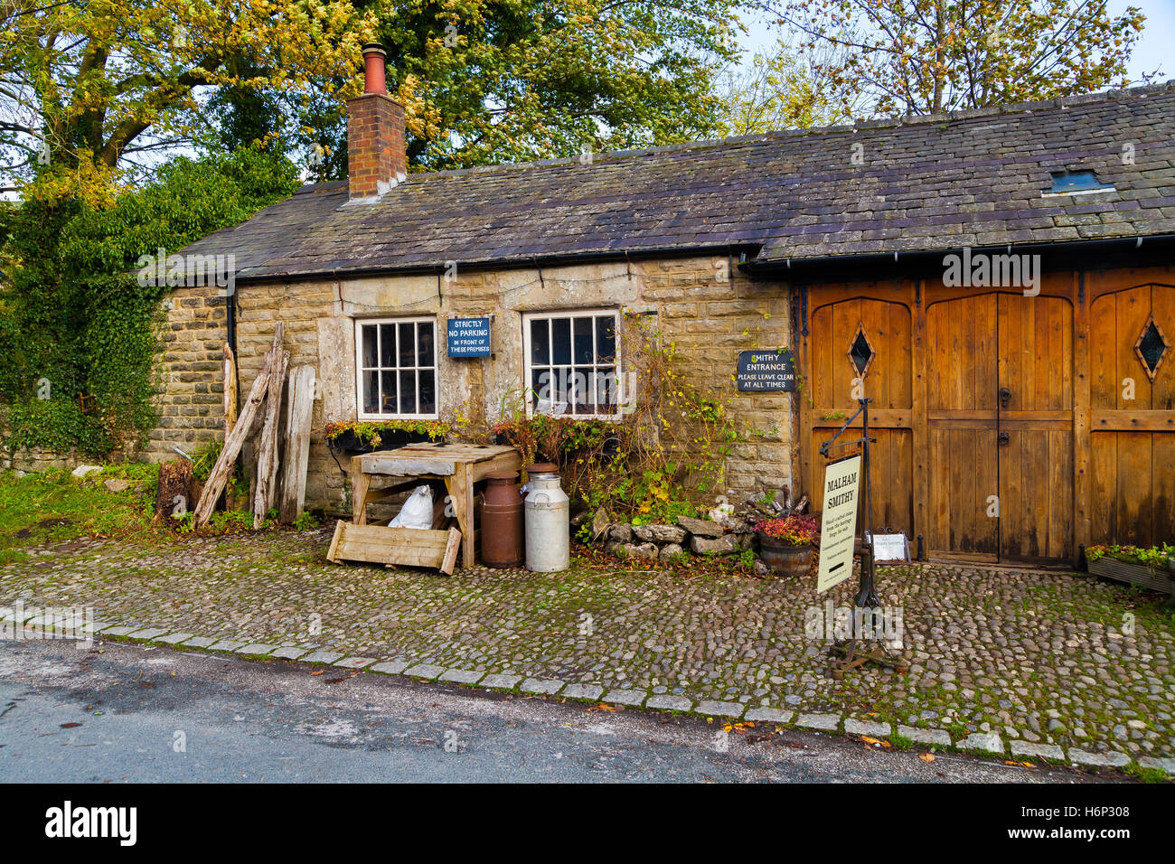 I fabbri workshop in Malham village, Yorkshire Dales, Inghilterra con vecchie urne di latte al di fuori su di ciottoli. Foto Stock