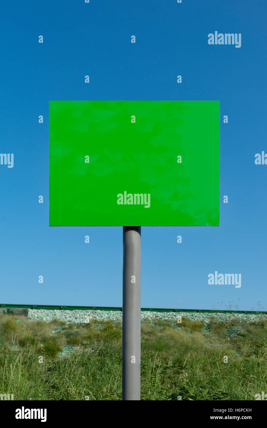 Immagine composita del vuoto segno verde sul polo grigia con terrapieno ferroviario e la linea in background contro un cielo blu chiaro su una soleggiata giornata estiva. Foto Stock