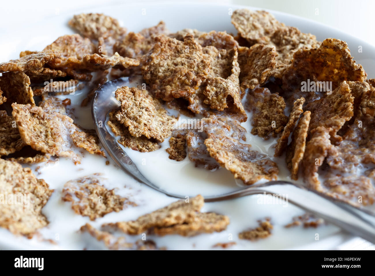 Dettaglio delle mezze mangiate di crusca di frumento Cereali per la prima colazione con il latte e il cucchiaio nella ciotola. Foto Stock