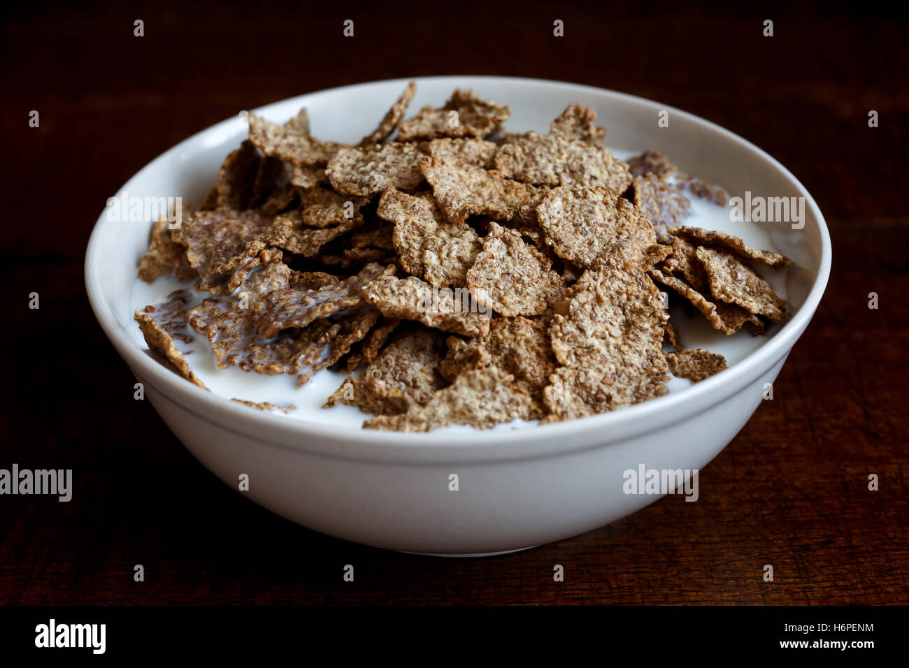 Crusca di frumento Cereali per la prima colazione con il latte nella tazza di ceramica. Moody illuminazione su scuro legno rustico superficie. Foto Stock