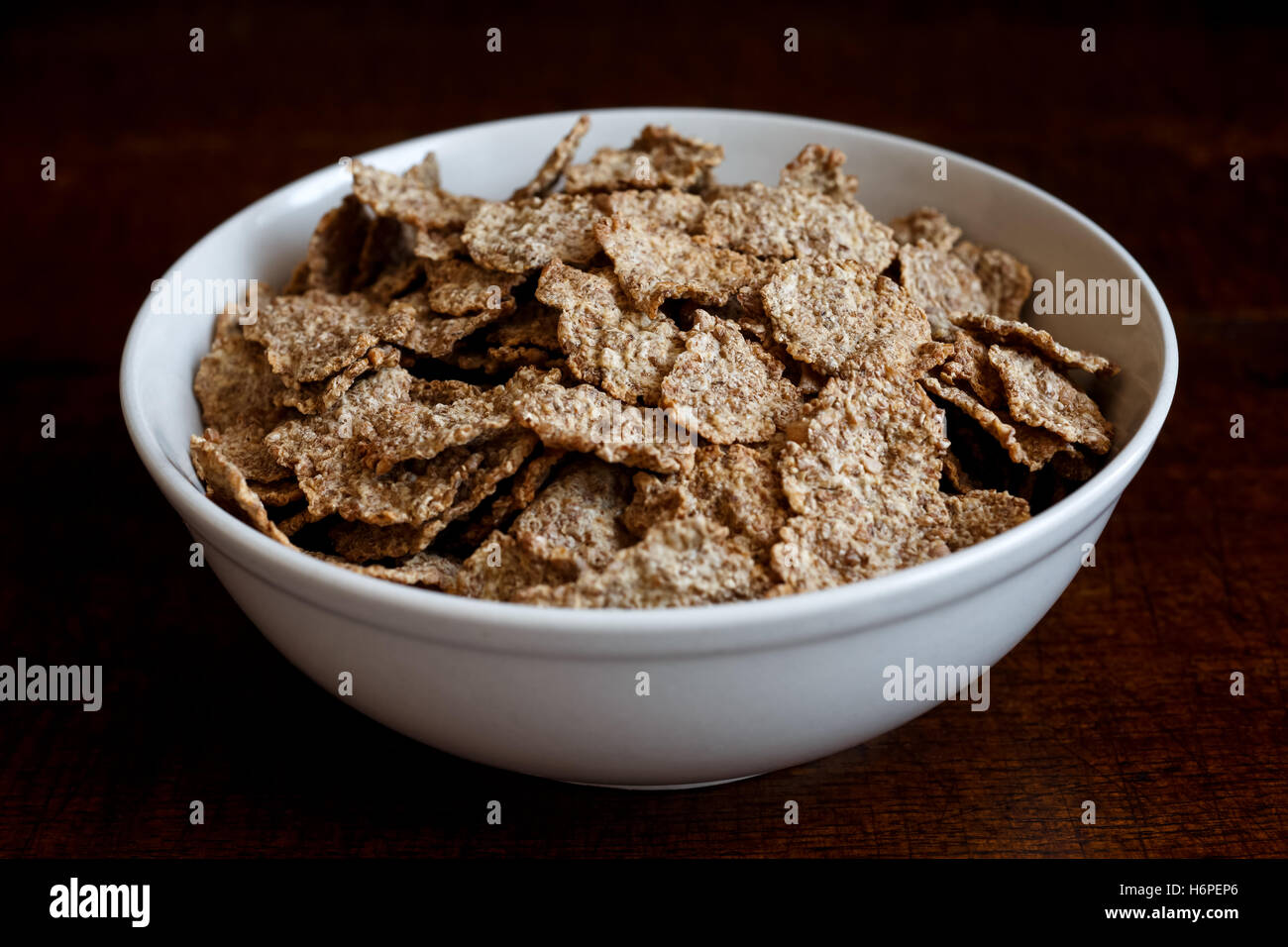 Crusca di frumento Cereali per la prima colazione con nessun latte nel recipiente di ceramica. Moody illuminazione su scuro legno rustico superficie. Foto Stock