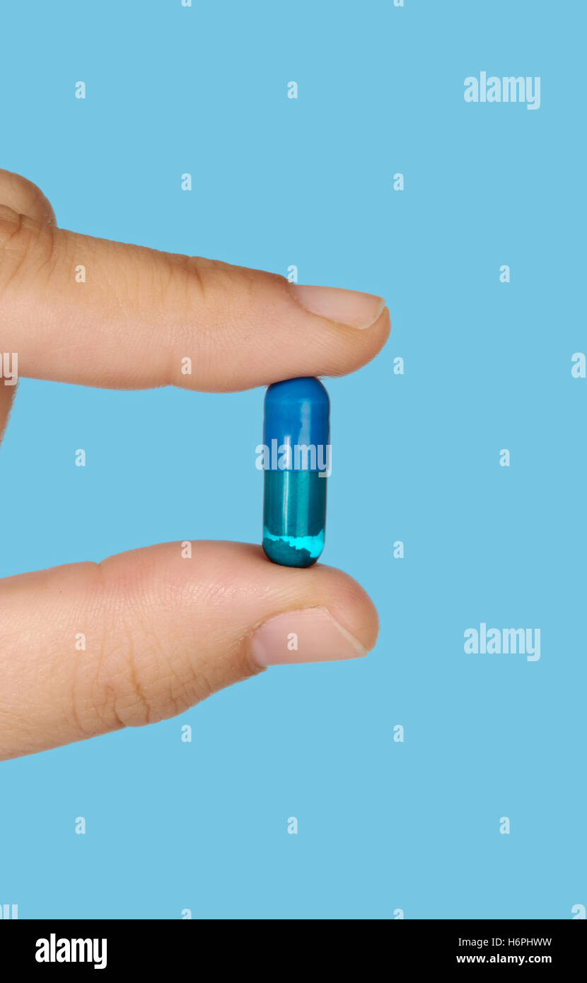 Mano che tiene una pillola farmaco su sfondo blu Foto Stock