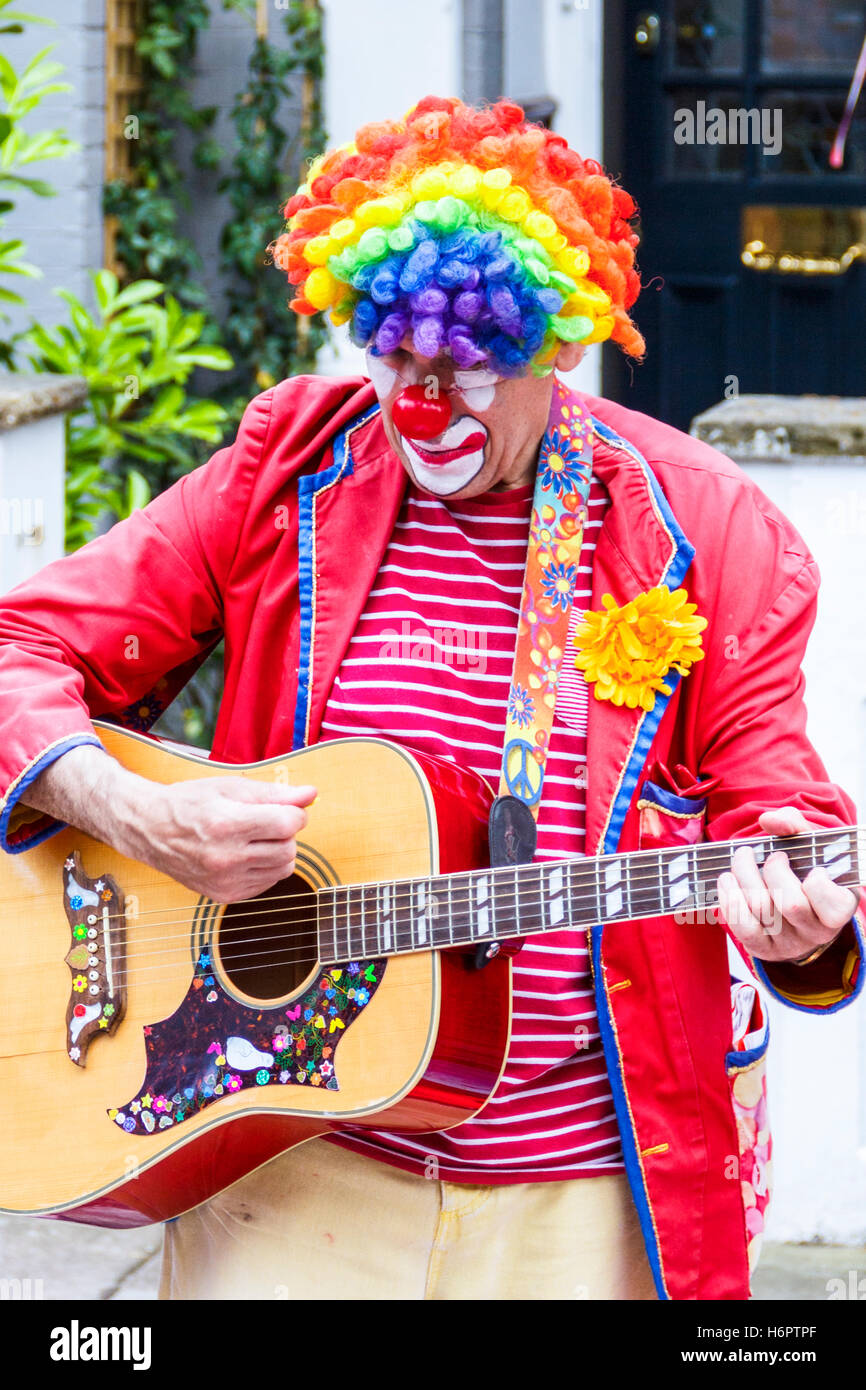 Un clown in un arcobaleno parrucca e giacca rossa a suonare la chitarra in corrispondenza di una parte di strada nella zona nord di Londra, Regno Unito Foto Stock