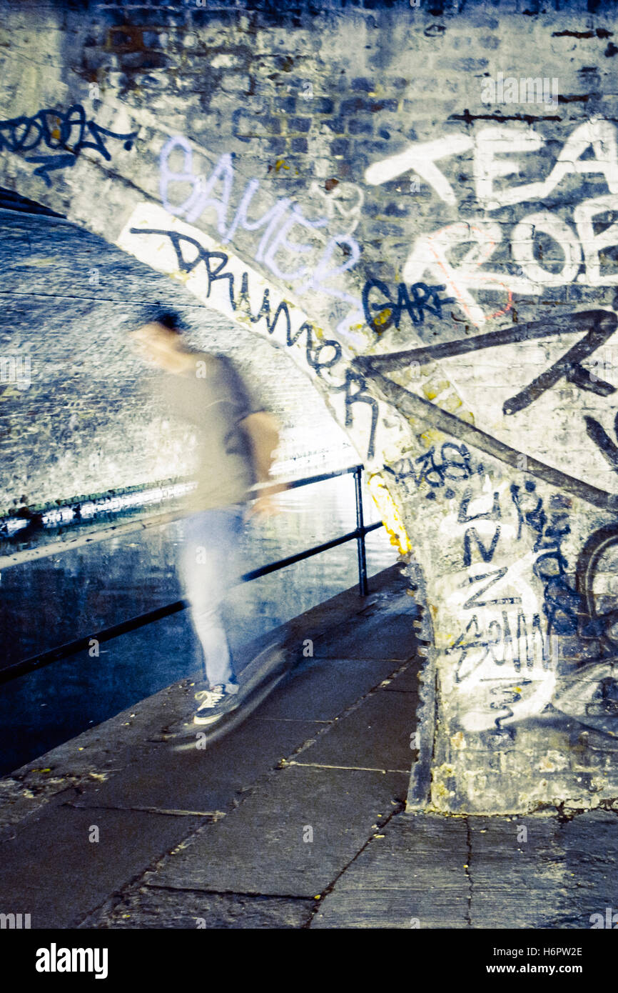 Un guidatore di skateboard uscente da sotto un ponte sopra la strada alzaia del Regent's Canal, St. Pancras, London, Regno Unito Foto Stock