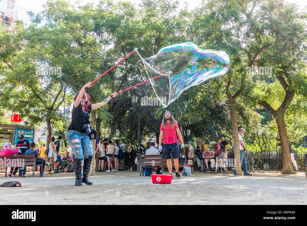 Un giovane di venti-qualcosa di donna spagnola enormi bolle di sapone in un parco vicino alla Sagrada Familia di Barcellona, Spagna. Foto Stock