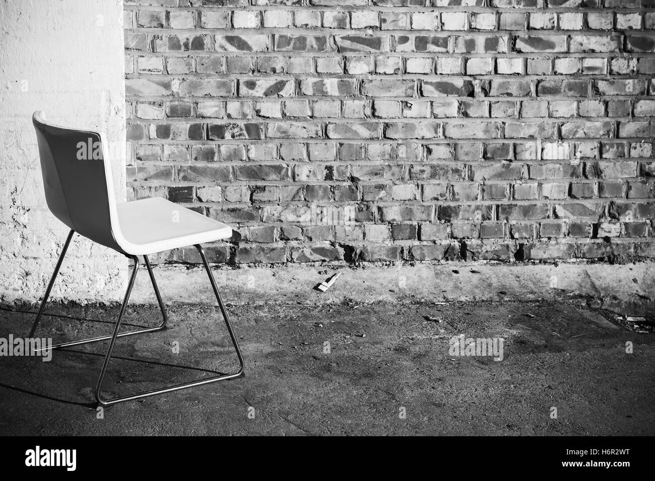Abstract interno vuoto sfondo bianco, sedia per ufficio sorge su un pavimento di cemento vicino a un muro di mattoni, foto in bianco e nero Foto Stock