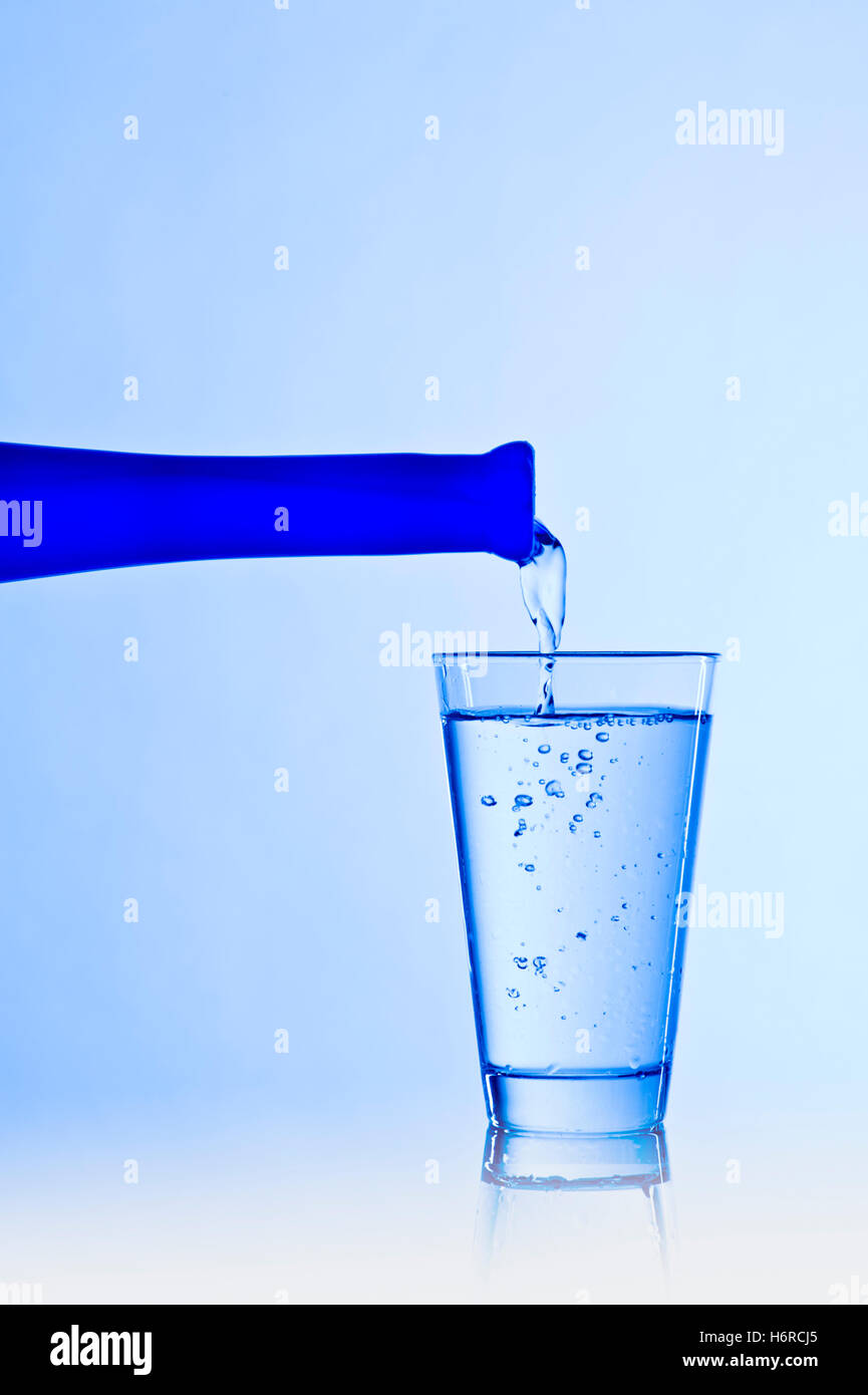 Bicchiere di acqua con una bottiglia di colore blu Foto Stock