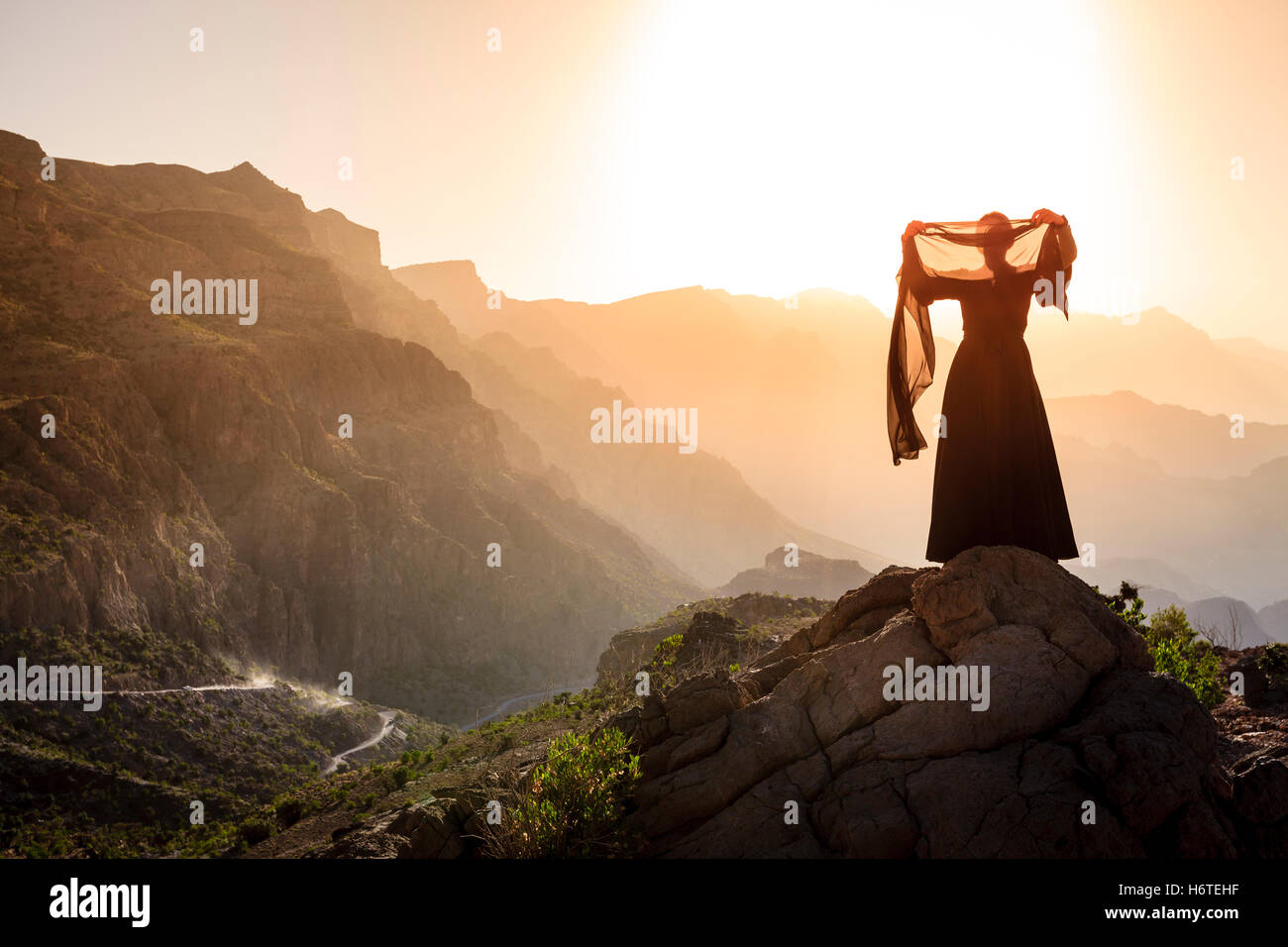 Lone donna in abaya in Al montagne Hajar di Oman al tramonto Foto Stock