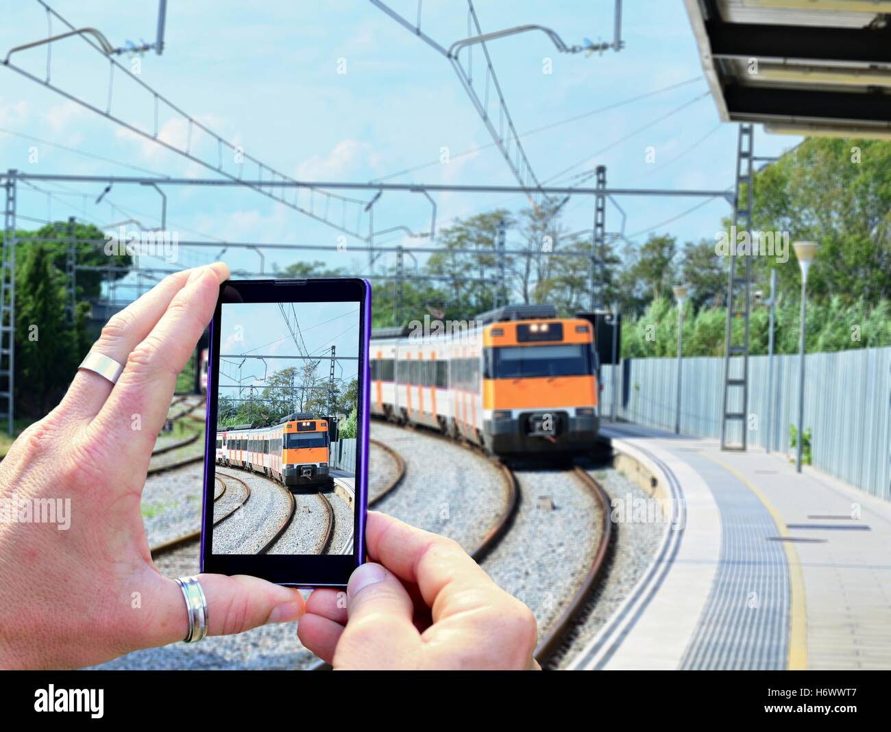 Vista sul telefono mobile display durante lo scatto di una foto di che arrivano in treno alla stazione ferroviaria. Tenendo il telefono mobile in han Foto Stock