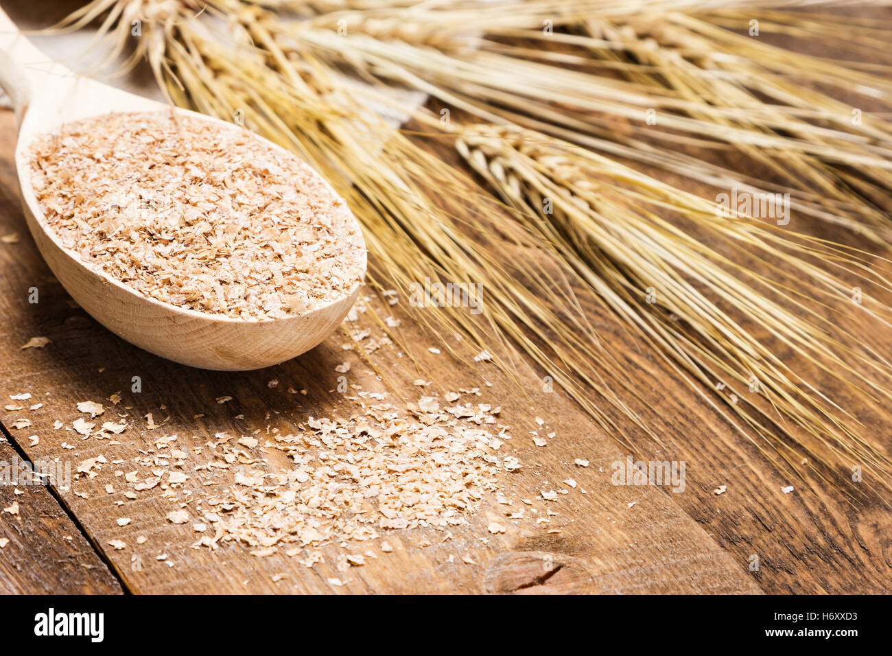 Close-up di crusca di frumento in cucchiaio di legno con spighe di grano. Integratore dietetico per migliorare la digestione. Fonte di fibra dietetica Foto Stock