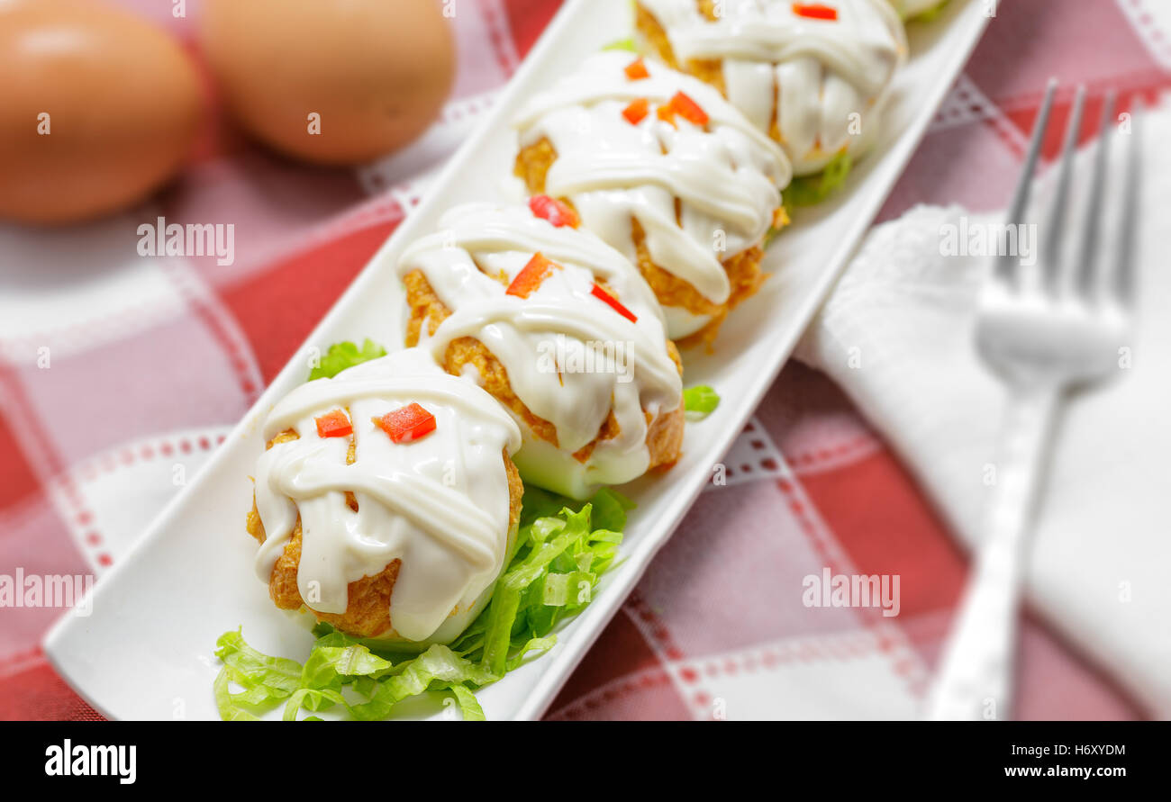 Uova ripiene con tonno, pomodoro, la maionese e il pepe rosso su sfondo bianco Foto Stock