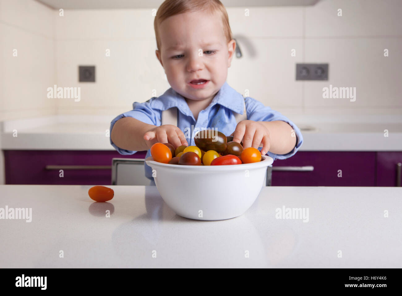 Baby boy giocando con maturi colorato di pomodori ciliegini. L'istruzione sulla nutrizione sana per bambini concept Foto Stock