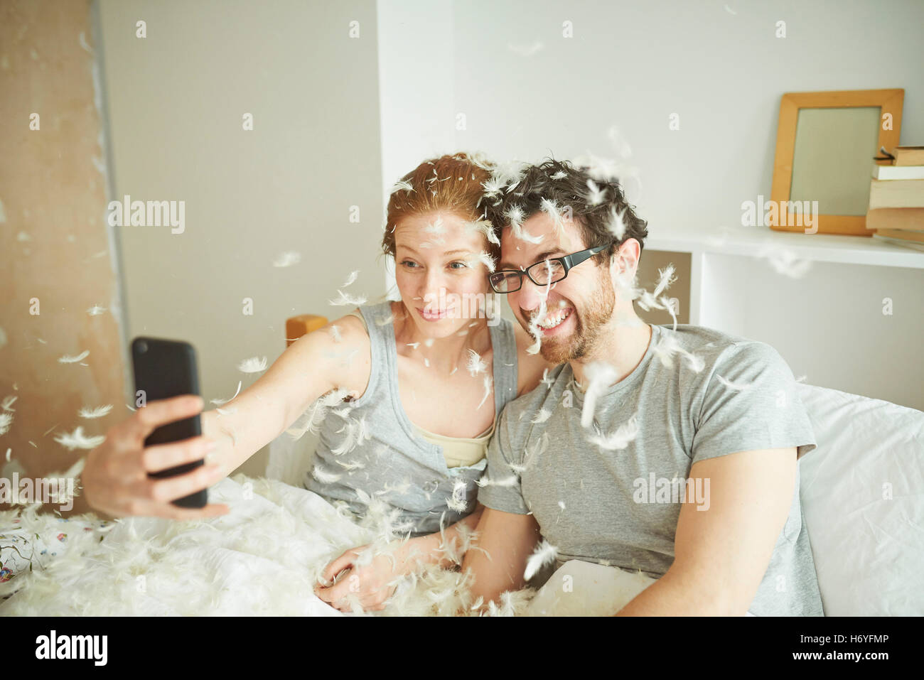 Metà adulto giovane contemplati nella lotta di cuscini di piume prendendo selfie smartphone nel letto Foto Stock