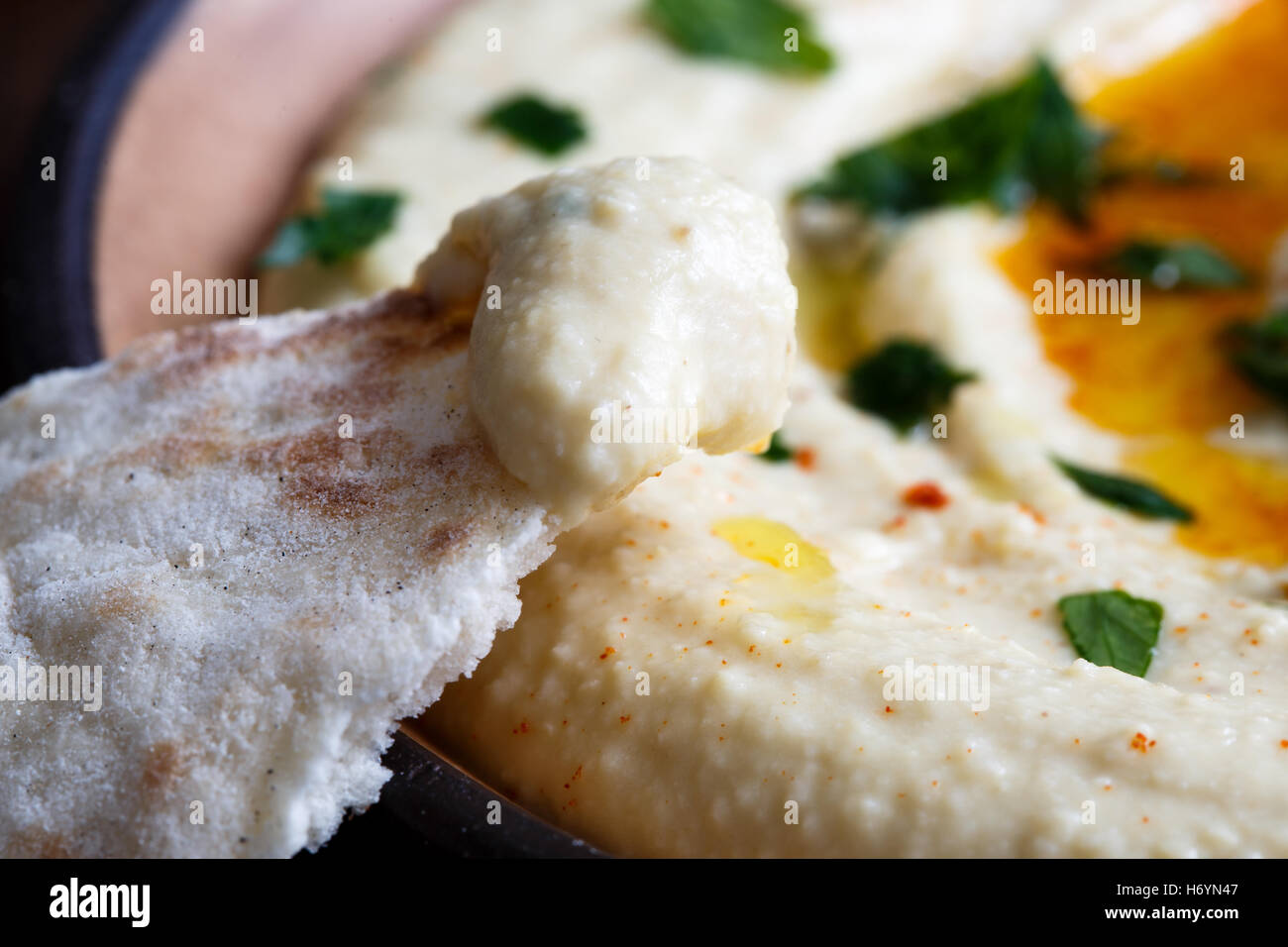 Dettaglio di hummus su pane pita. Piatto di hummus in background. Foto Stock