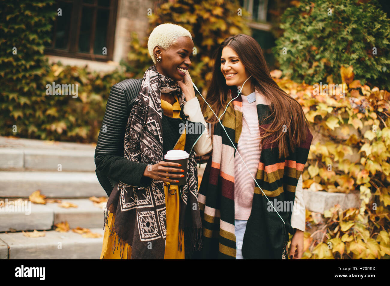 Americano africano e caucasici che pongono la donna fuori con il telefono cellulare e una tazza di caffè per andare in autunno Foto Stock