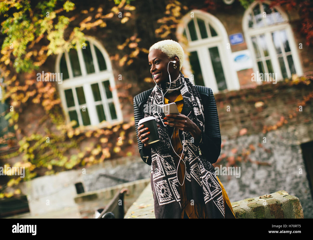 African American donna ascoltare musica all'aperto e tenendo il caffè per andare Foto Stock