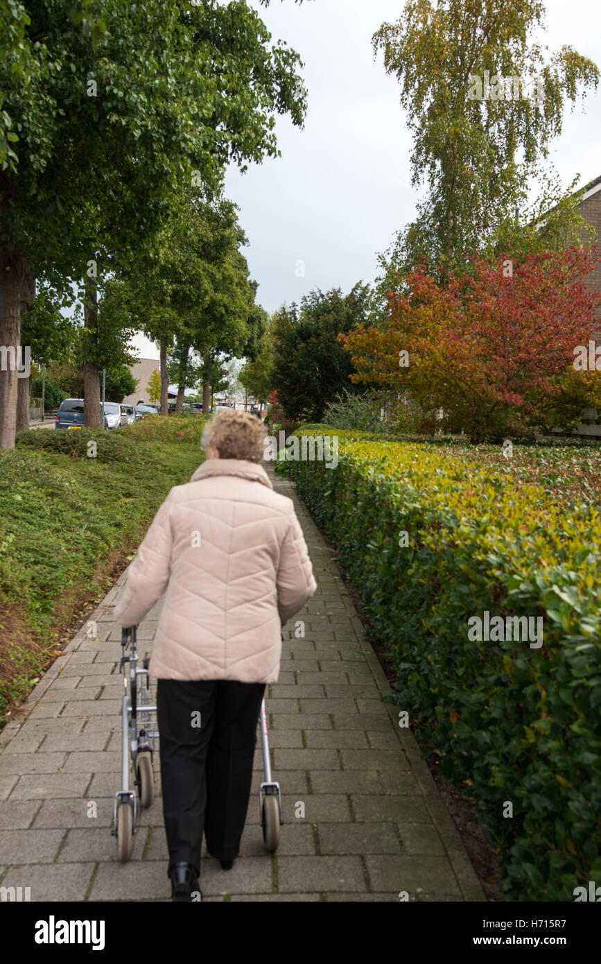Vecchia donna con assistere camminando sul marciapiede Foto Stock