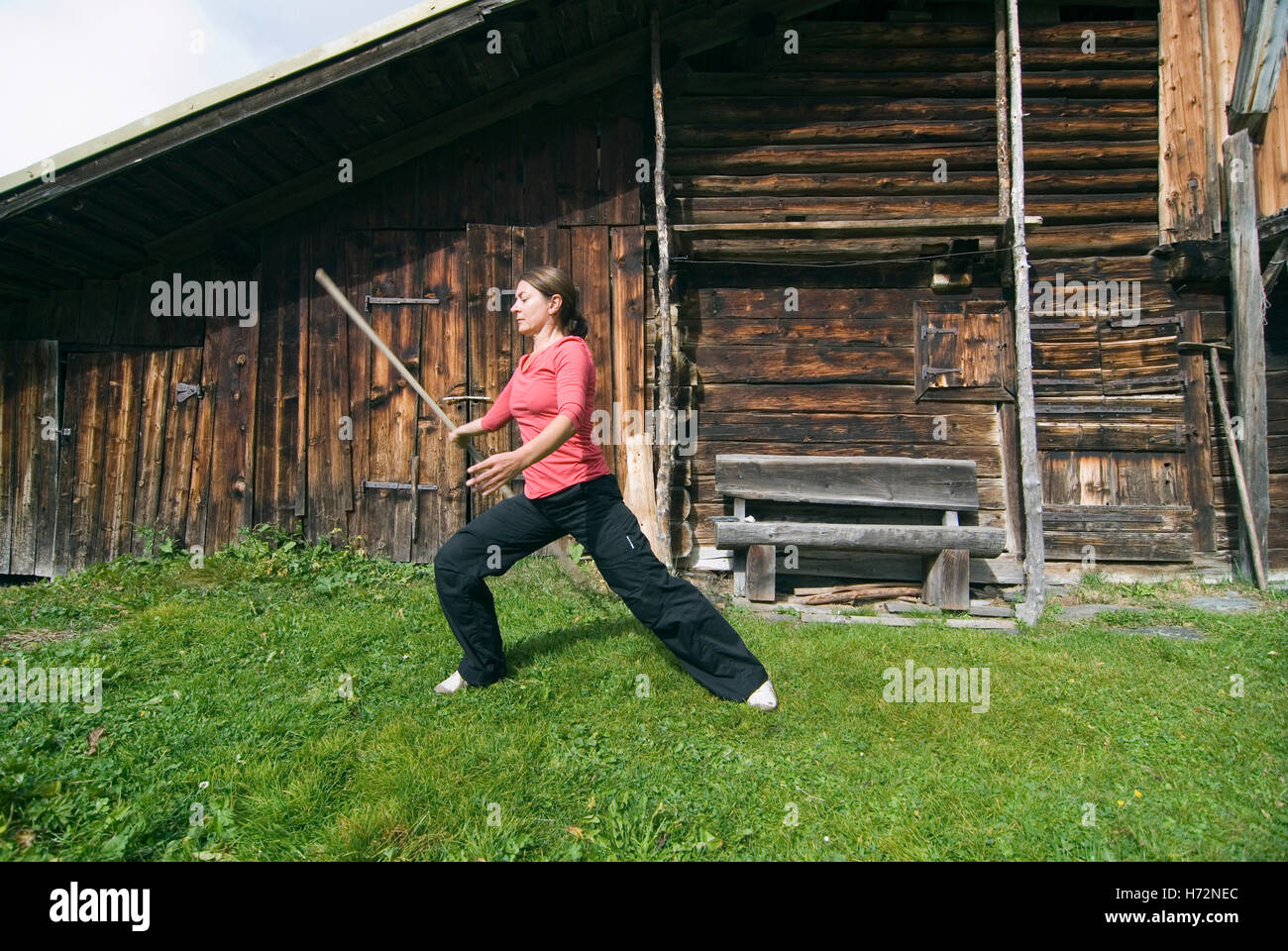 Donna, inizio 40s, facendo Tai Chi davanti a una capanna in legno nelle alpi svizzere, Svizzera, Europa Foto Stock