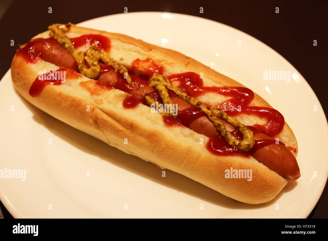 Un fresco hotdog alla griglia su un panino con un flusso di senape e ketchup su una piastra Foto Stock