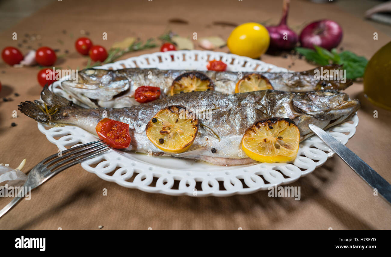 Trota di delizioso pesce al forno con limone, pomodori e spezie Foto Stock