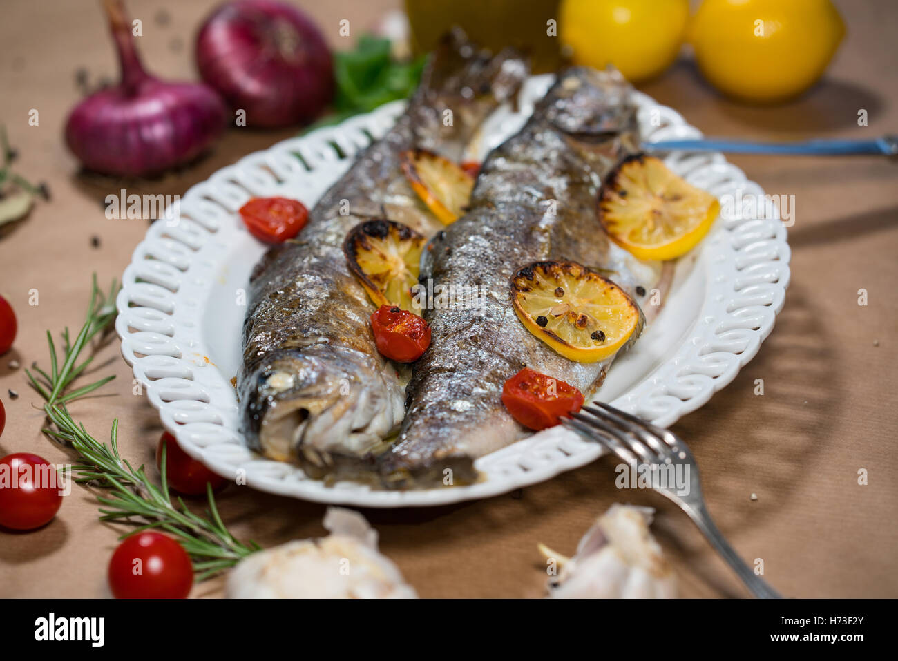Trota di delizioso pesce al forno con limone, pomodori e spezie Foto Stock