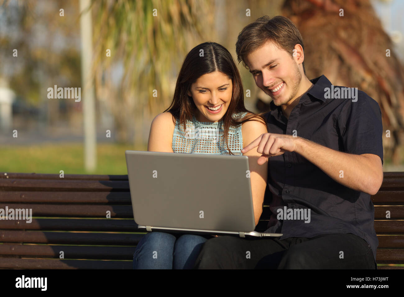 Giovane guardare i media in un notebook seduta su una panchina Foto Stock