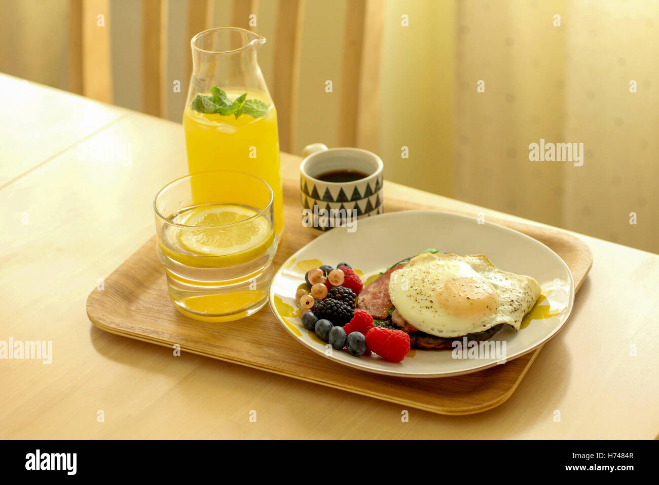 Pasto sano con uovo fritto, bacche, acqua, succo di limone e caffè su un vassoio Foto Stock