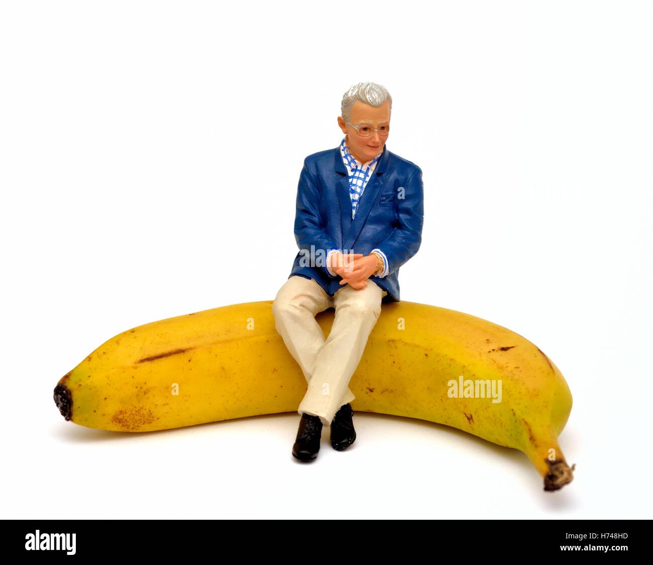 Una figurina pensionato maschile seduto su una banana. Foto Stock