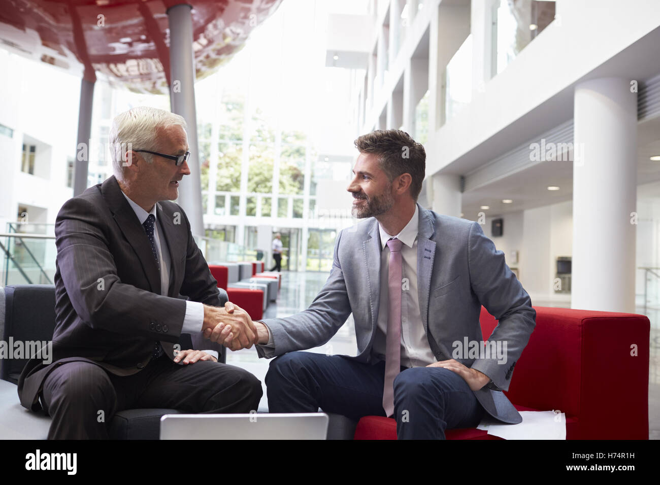 Due imprenditori stringono le mani nella lobby dell ufficio moderno Foto Stock