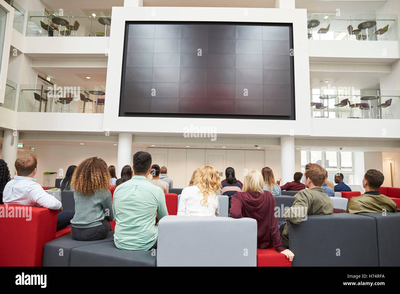 Gli studenti a guardare grande schermo in università atrium, vista posteriore Foto Stock
