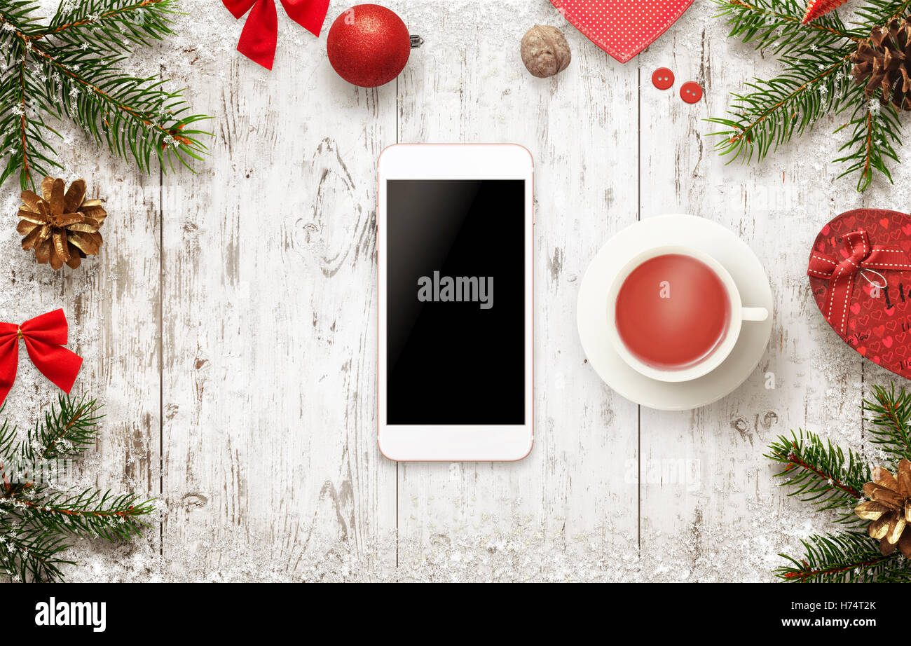 Smart phone con decorazioni di Natale sulla tavola. Bere il tè e una pausa nelle giornate invernali. Visualizzazione isolata del dispositivo mobile Foto Stock