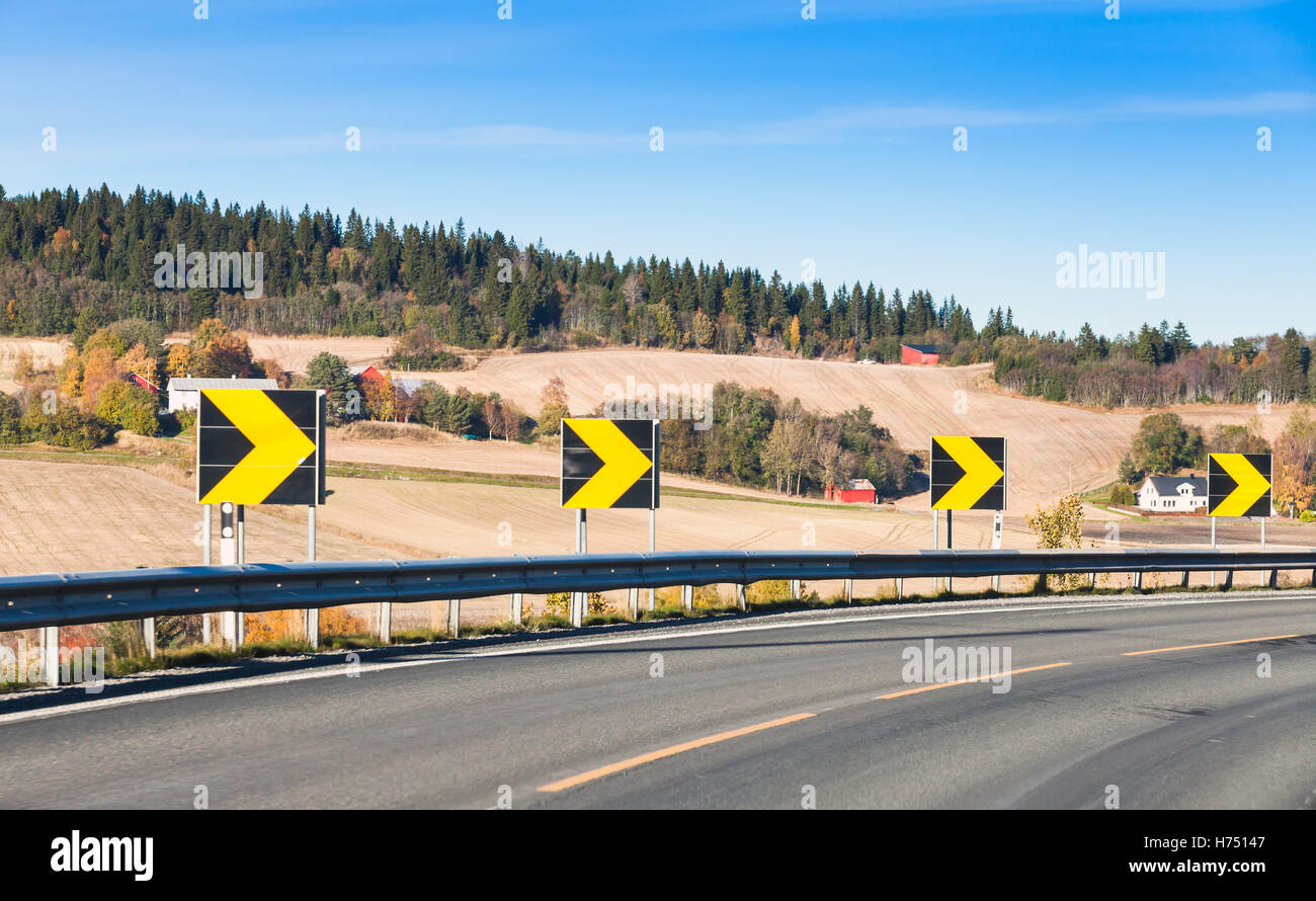 Curva pericolosa. Le frecce gialle in quadrato nero cartelli lungo girando autostrada, rurale strada norvegese Foto Stock