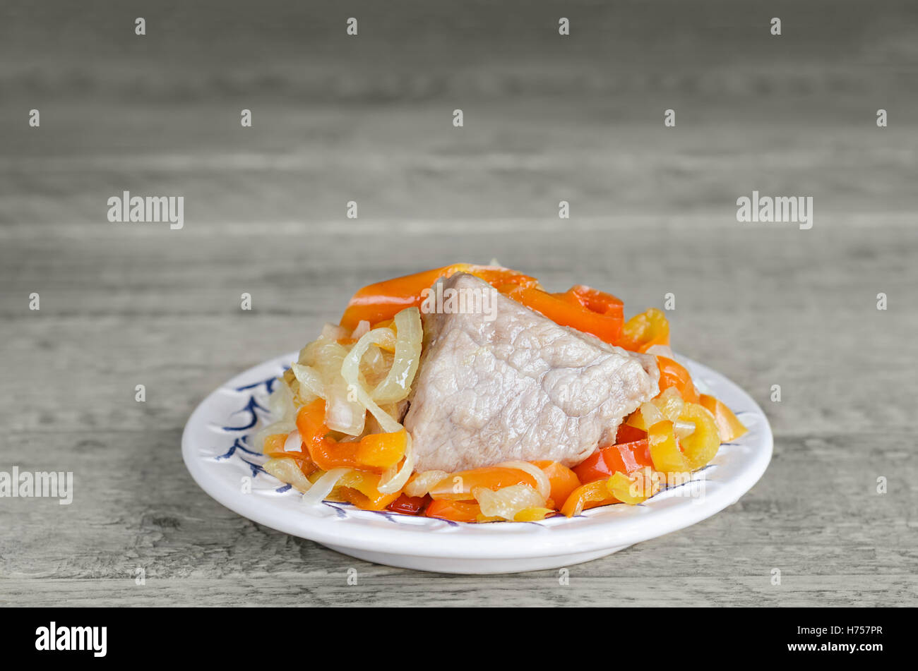 Pezzo di carne di maiale con verdure sulla piastra, il grigio superficie di legno. Foto Stock