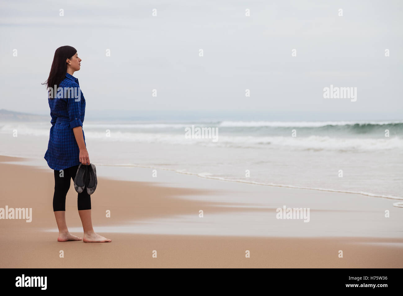Solitaria e premuto donna guardando il mare in una spiaggia deserta in una giornata autunnale. Foto Stock