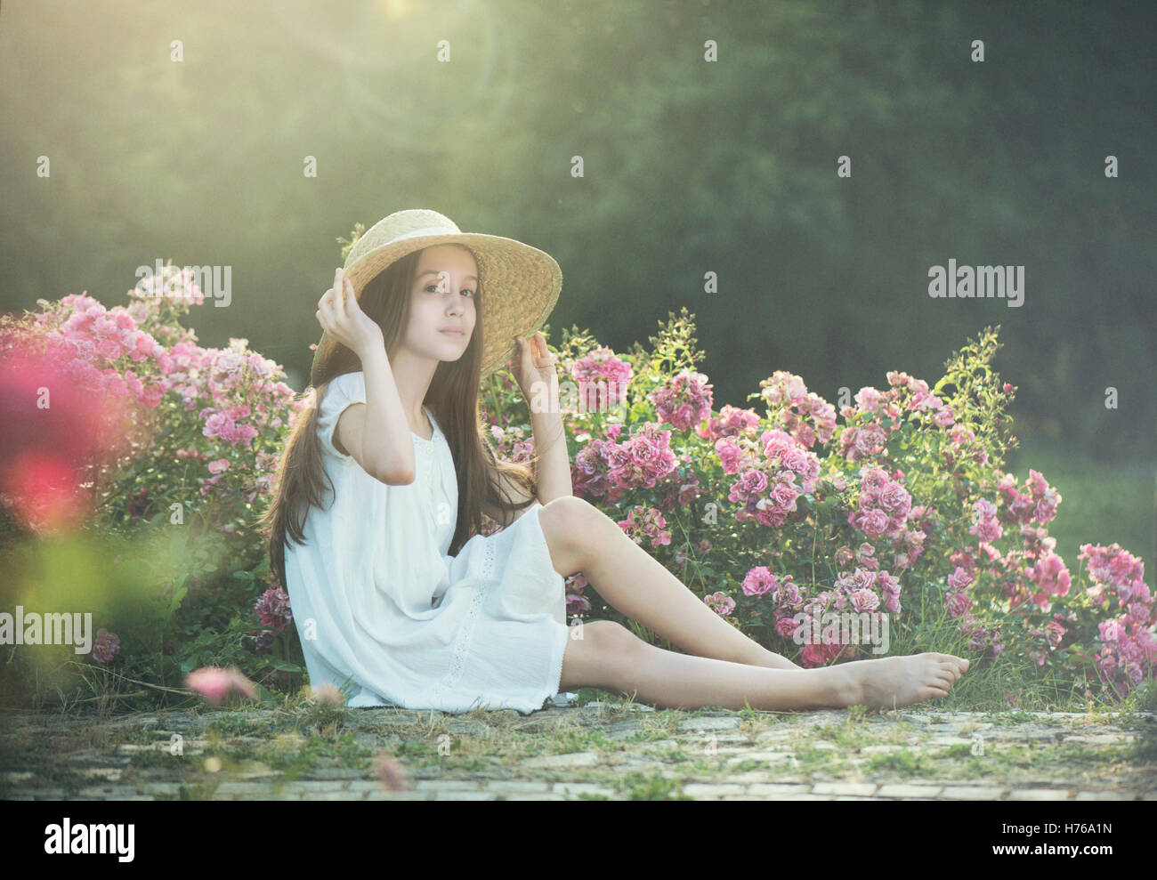 Ritratto di una ragazza seduta da rose in giardino Foto Stock