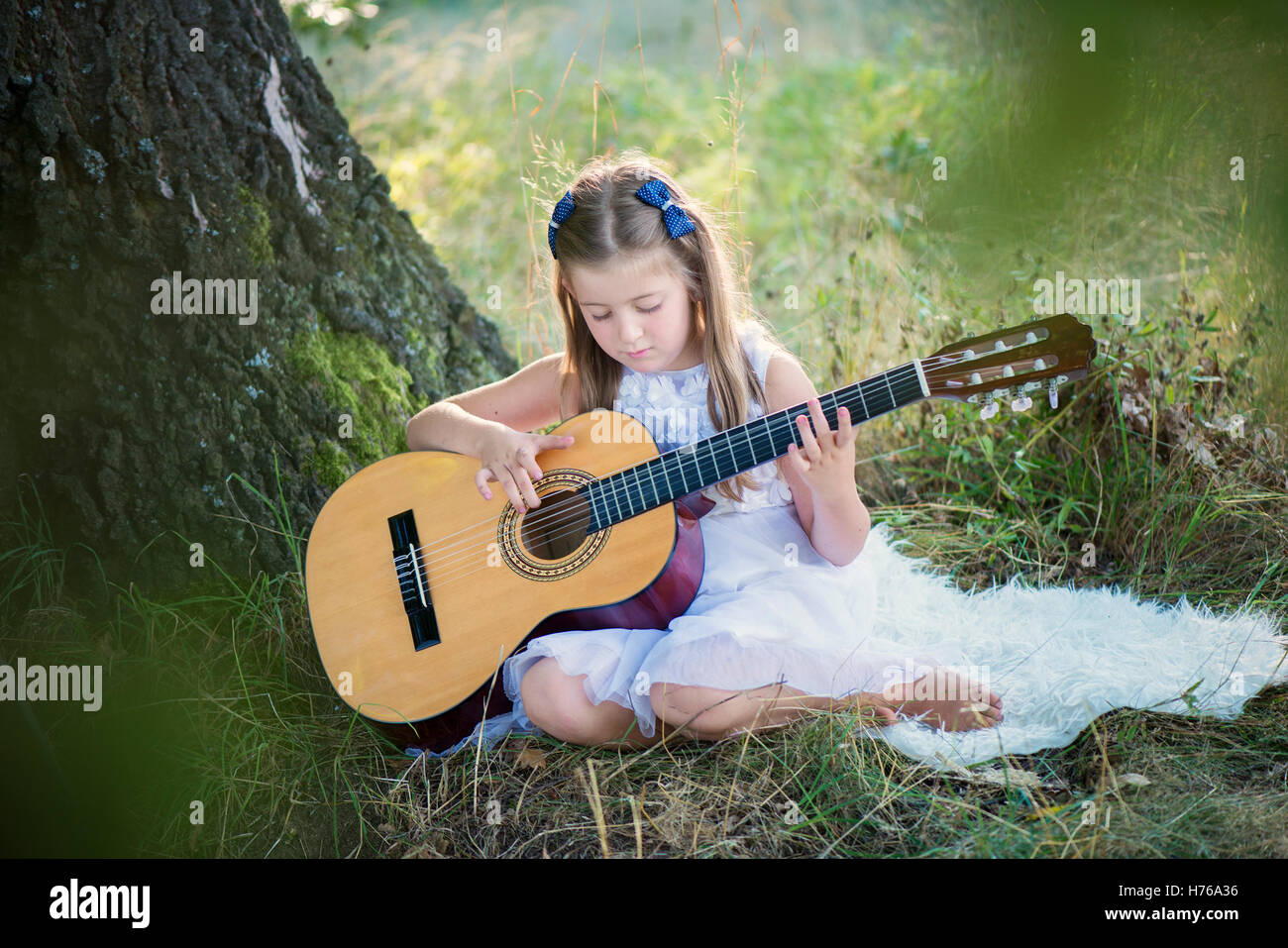 Ragazza seduta nella foresta a suonare la chitarra Foto Stock