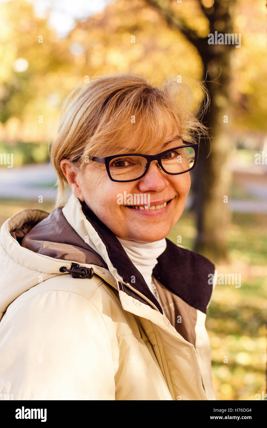 Carino donna matura con gli occhiali in autunno park Foto Stock