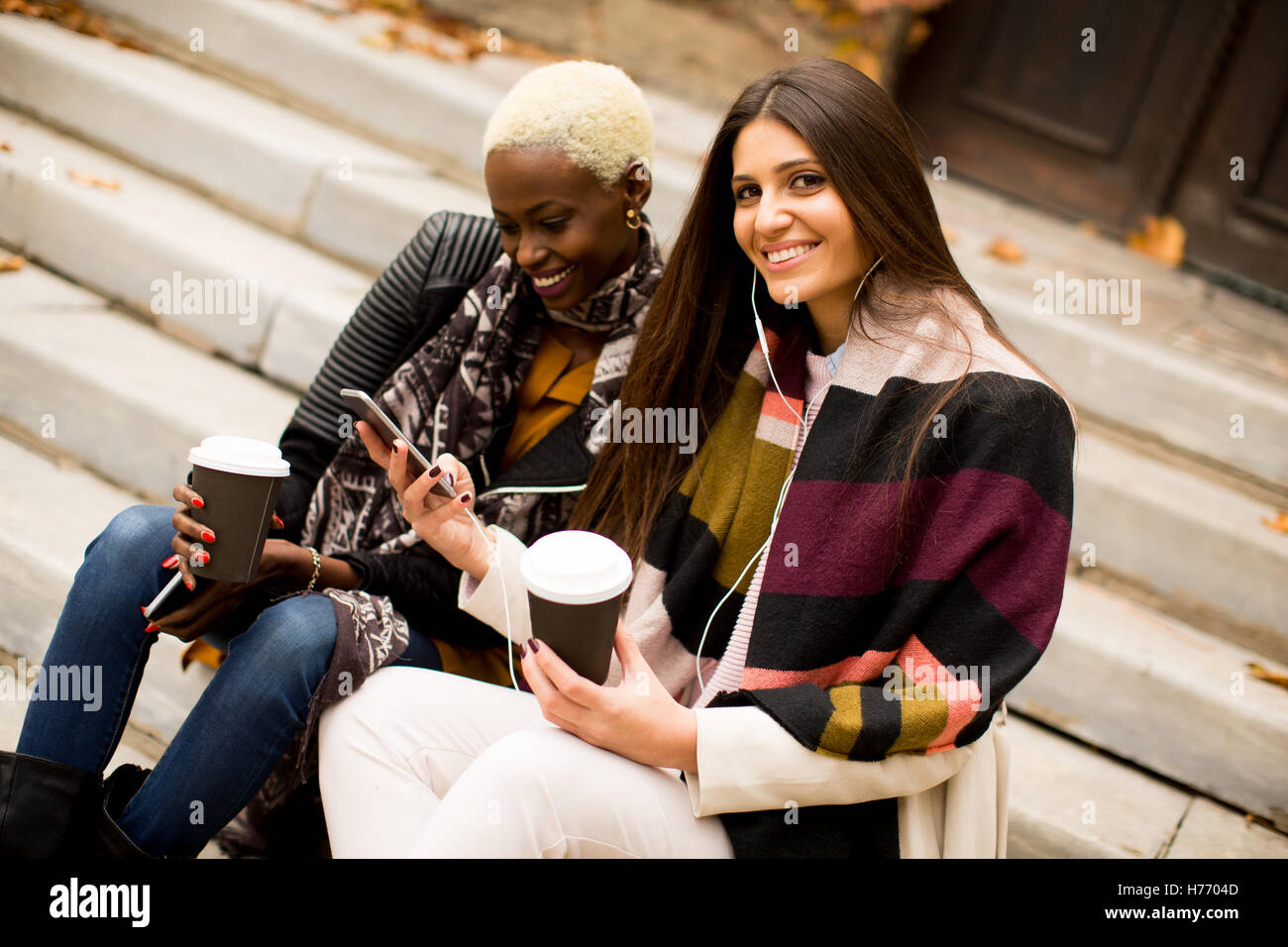 Americano africano e caucasici che pongono la donna fuori con il telefono cellulare e una tazza di caffè per andare in autunno Foto Stock
